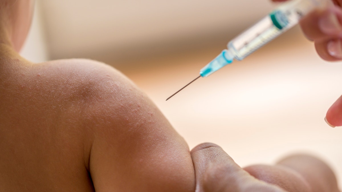 Doctor injecting a young child with a vaccination or antibiotic in a small disposable hypodermic syringe, close up of the kids arm and needle.