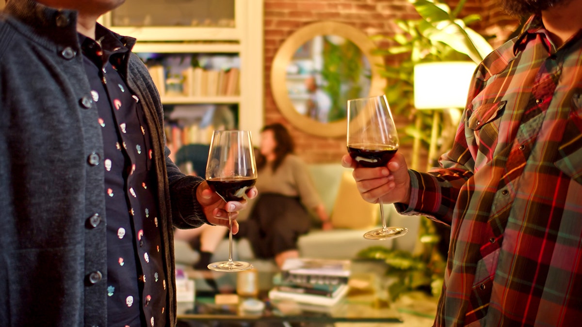 two men hold glasses with red wine at a dinner party