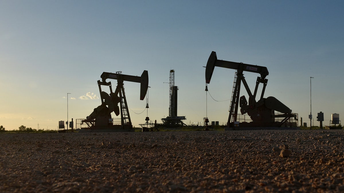 Pump jacks operate in front of a drilling rig in an oil field in Midland, Texas.