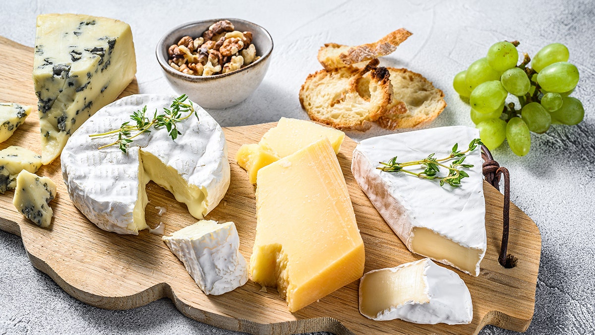 Assorted cheeses, nuts, bread, and grapes on a wooden cheese board.
