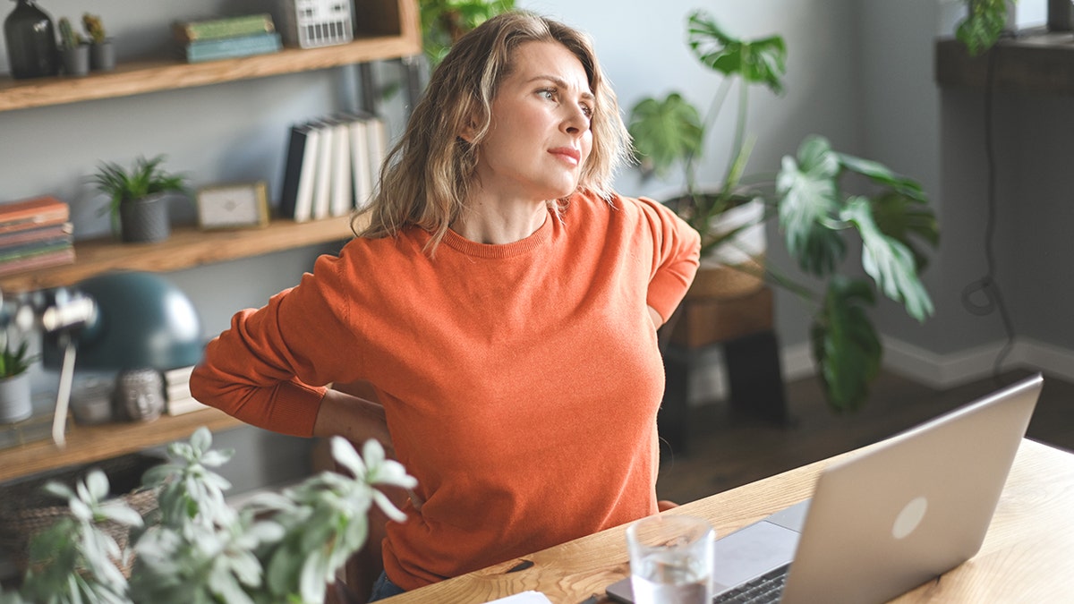 adult woman with back pain sits at desk