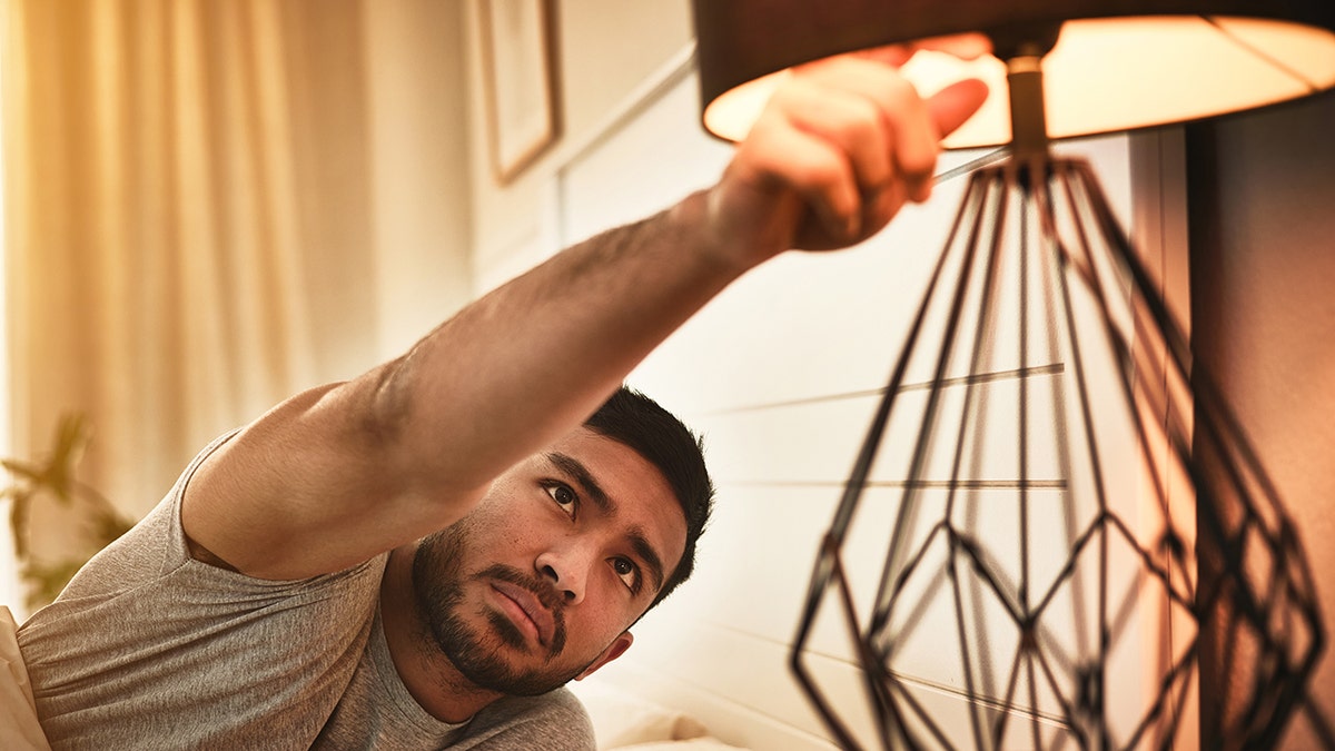 Man switches off the lamp light in bedroom before sleeping.