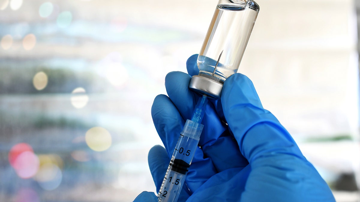 Medical personnel filling a syringe needle with generic vaccine booster from vial
